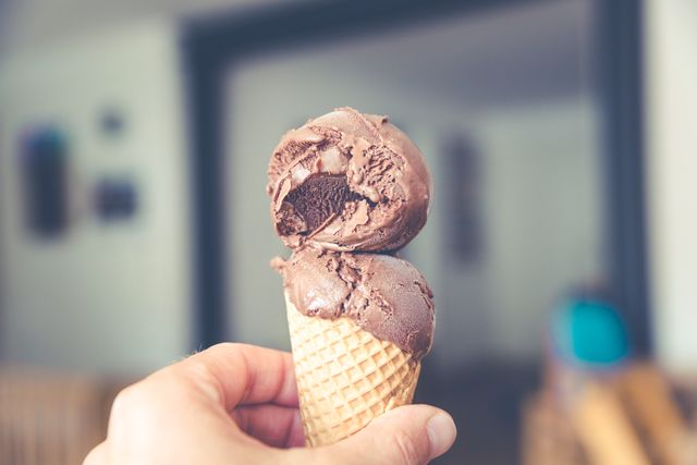 Delightful image capturing a hand holding a double scoop of rich chocolate ice cream in a waffle cone. This indoor setting emphasizes the enjoyment of a classic sweet treat. Ideal for use in food blogs, dessert menus, ice cream shop advertisements, and culinary magazines promoting indulgent desserts or homemade ice cream recipes.