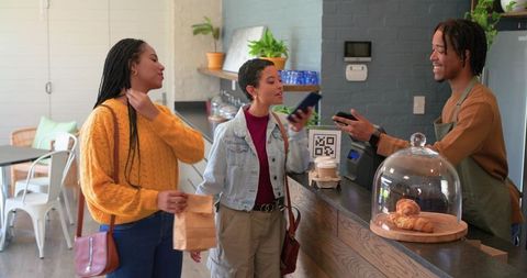Contactless mobile payment at cozy urban cafe with smiling barista and friends ordering