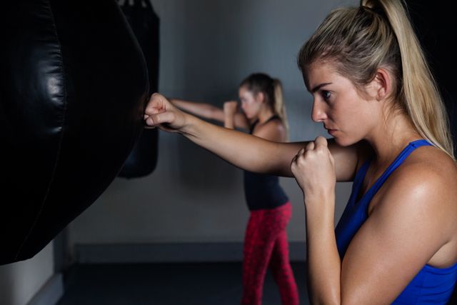 Women practicing boxing in a fitness studio, focusing on punching bags. Ideal for promoting fitness, strength training, and active lifestyle. Useful for gym advertisements, fitness blogs, and health-related content.