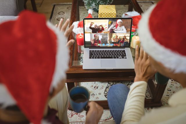 Couple wearing santa hats waving at friends on a screen, connected through a laptop during Christmas. Ideal for illustrating virtual holiday events, family connectivity during festive seasons, and the use of technology to bridge distances. Suitable for websites, blogs, articles about remote celebrations, and technology in holidays.