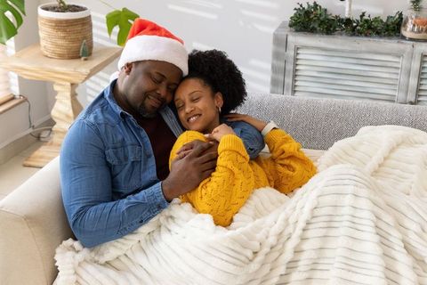 African american couple cuddling on sofa with santa hat and cozy blanket holiday morning