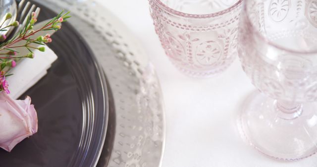 Elegant table setting features a black plate and delicate glassware, with copy space. A touch of floral decor adds a fresh accent to the sophisticated dining arrangement.