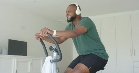 Man cycling on upright exercise bike at home wearing headphones and smartwatch