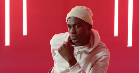 Stylish afro american man in neon lit room with beanie and hoodie