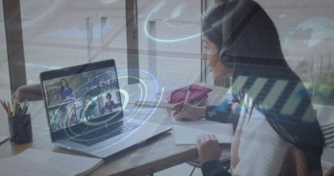 High school student taking online math lesson at home desk, writing notes, wearing headphones