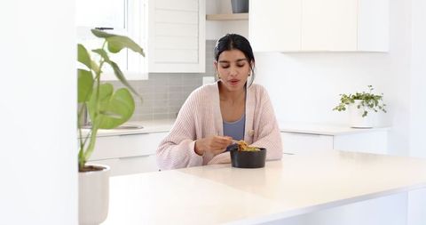 Woman eating noodles at modern kitchen island