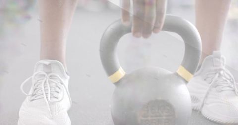 Male athlete preparing and gripping 16kg kettlebell between white sneakers low-angle closeup