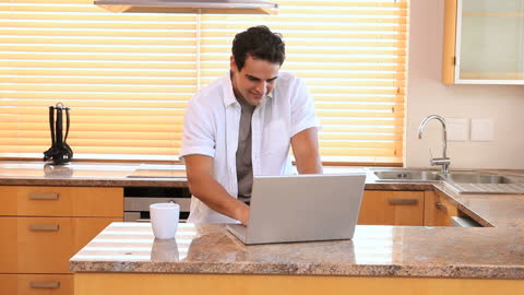 Man Enjoying Coffee While Working on Laptop in Modern Kitchen