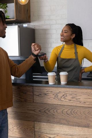 African-american barista serving coffee as customer tapping smartwatch to pay