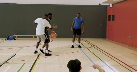 Indoor basketball players practicing dribbling and defense on hardwood gym court