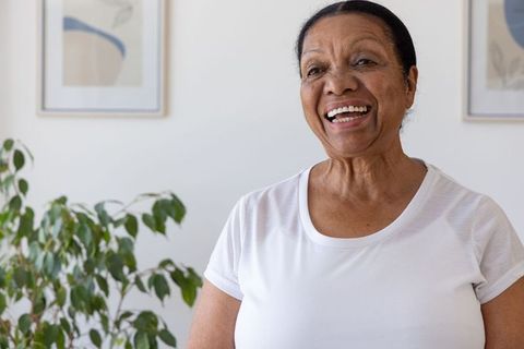 Senior woman smiling and standing in bright minimalist interior with houseplant