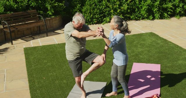 Seniors balancing on yoga mats in a sunny garden surrounded by greenery. This can be used for health and wellness articles, senior fitness programs, and representations of active aging.