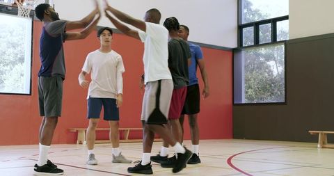 Diverse male basketball team high-fiving and starting drills in indoor training session