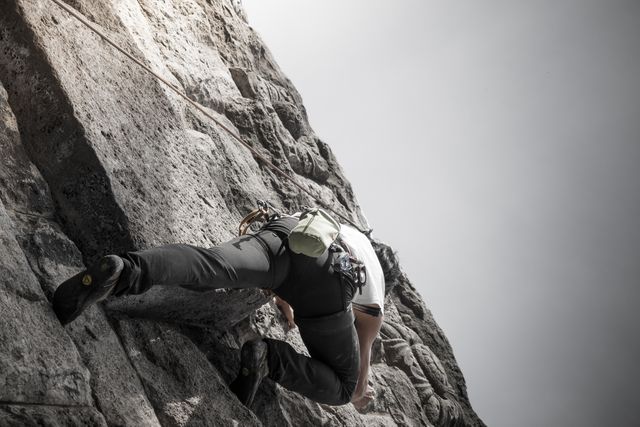 Man climbing a steep rock face outdoors. Ideal for topics on extreme sports, adventure, and physical fitness. Useful for promoting outdoor clothing brands, adventure tours, and fitness programs.