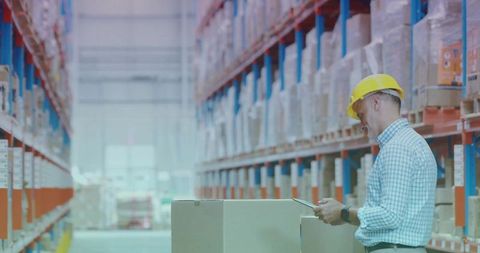 Warehouse supervisor inspecting pallets with tablet in high-bay distribution aisle