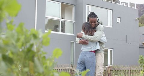 African American man and Indian woman embracing in garden by modern gray home