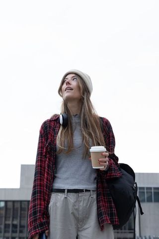 Young commuter standing with coffee and backpack wearing beanie and plaid shirt