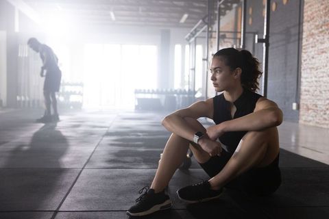Athletic woman resting after workout in industrial gym with kettlebell and smartwatch