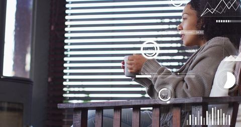 Contemplative woman sipping mug on wooden chair by blinds with floating data hud overlays