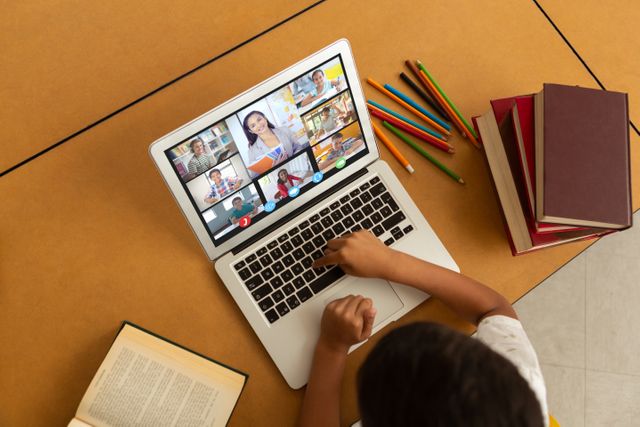 Child engaged in online classes via laptop. Books and pencils are on the table for school activities. Suitable for illustrating remote learning, homeschooling, virtual classrooms, and the integration of technology into education.