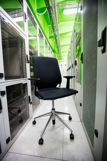 Empty office chair positioned in the corridor of a modern server room with visible server racks and equipment. Ideal for illustrating concepts related to IT infrastructure, data centers, technology workplaces, and professional environments.
