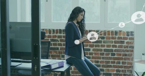 Indian woman using tablet while sitting on desk in brick office with digital overlay, open-plan