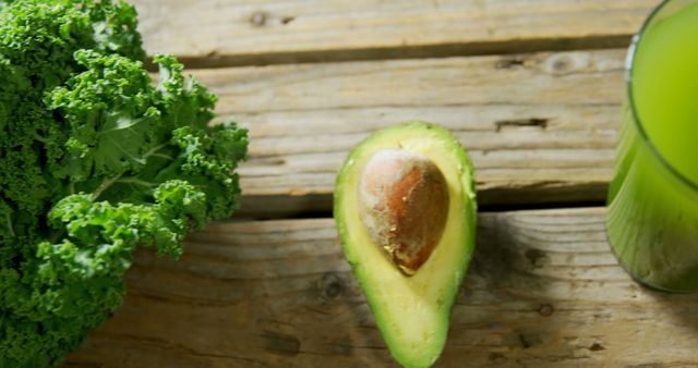A ripe avocado sits next to fresh kale and a green smoothie on a rustic wooden table, with copy space. These nutritious ingredients are often used in healthy eating and diet plans for their vitamins and minerals.