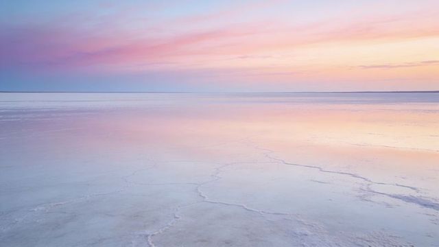 Pastel sunrise over glassy salt flats reflecting pink blue skies with cracked salt texture