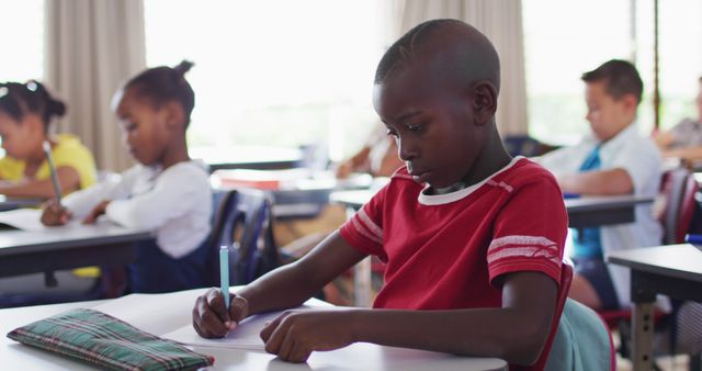 Portrait of african american schoolboy sitting in classroom, making notes. children at primary school in summer.