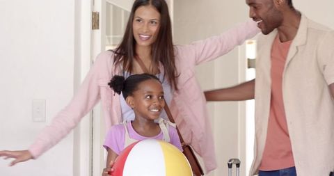 Smiling family entering home with beach ball and luggage