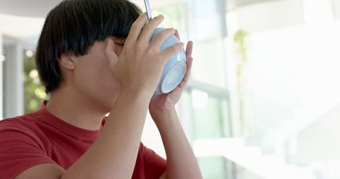 Asian Student Drinking from Cup in Relaxed Home Environment
