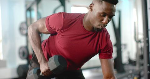 African american man performing bent-over one-arm dumbbell row in modern gym