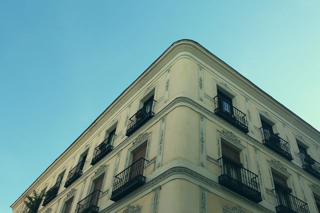 This photo showcases the corner of a multi-story building with ornate balconies under a clear sky, ideal for use in urban development, real estate promotions, or architectural design websites. The crisp lines and bright daylight emphasize modern urban living.