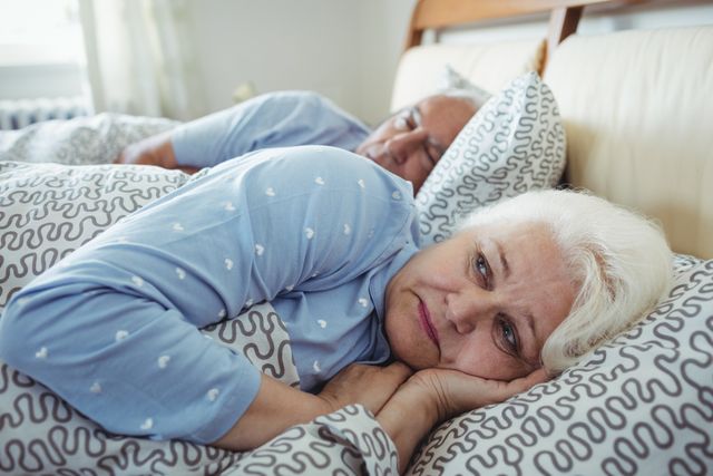 Senior man sleeping while woman still awake on bed in bed room