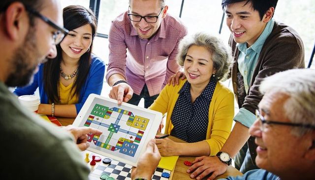 Multigenerational group sharing digital board game on tablet, laughing and collaborating