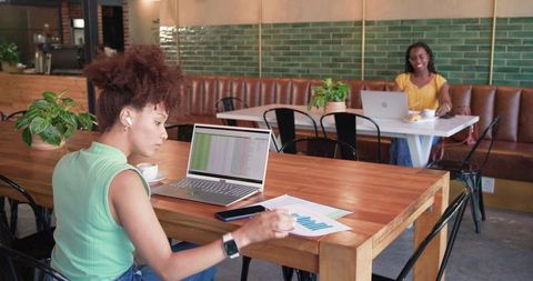 Working remotely at coffeehouse: woman checking spreadsheet and chart on laptop