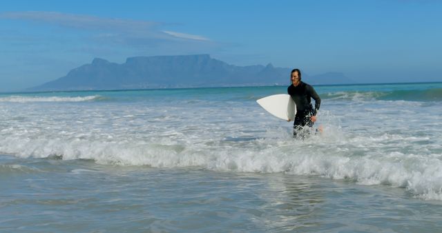 Young Caucasian man enjoys surfing at the beach, with copy space. He's exiting the water with his surfboard, showcasing an active lifestyle outdoors.