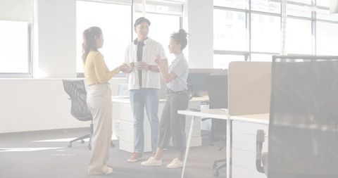 Three coworkers chatting in modern open-plan office during casual coffee break