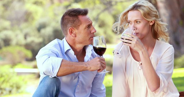 A middle-aged Caucasian couple enjoys a romantic moment with a glass of wine in an outdoor setting, with copy space. Their relaxed postures and eye contact suggest a comfortable and intimate connection.