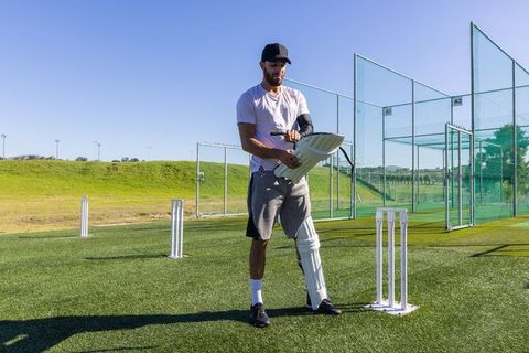 Cricket player adjusting batting pad at outdoor nets on sunny practice field for training