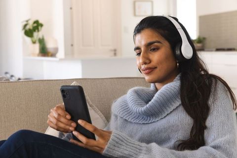 Woman using smartphone and headphones in cozy home interior