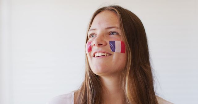 Young woman captured smiling with French flag face paint. Ideal for use in articles and websites discussing national pride, patriotism, cultural celebrations, or sports events. Can also be used in promotional materials surrounding international events and celebrations.