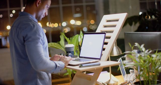 Focused Man Working on Laptop at Standing Desk in Modern Office with City Lights - Download Free Stock Images Pikwizard.com