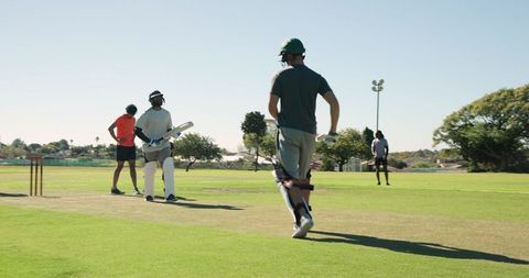 Community cricket players batting, running on sunny suburban grass pitch with helmet