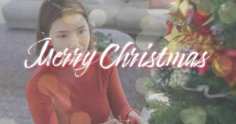 Woman decorating christmas tree in red sweater with cozy bokeh merry christmas overlay