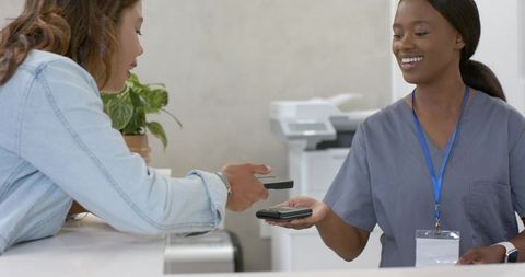 Healthcare receptionist accepting contactless smartphone payment at clinic counter