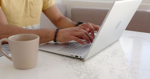Typing hands using laptop on marble table with ribbed coffee mug in natural daylight