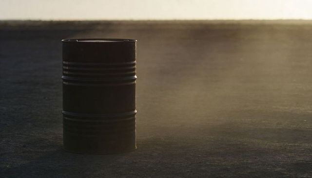 Backlit Ribbed Metal Barrel Casting Long Shadow on Dusty Asphalt at Dusk