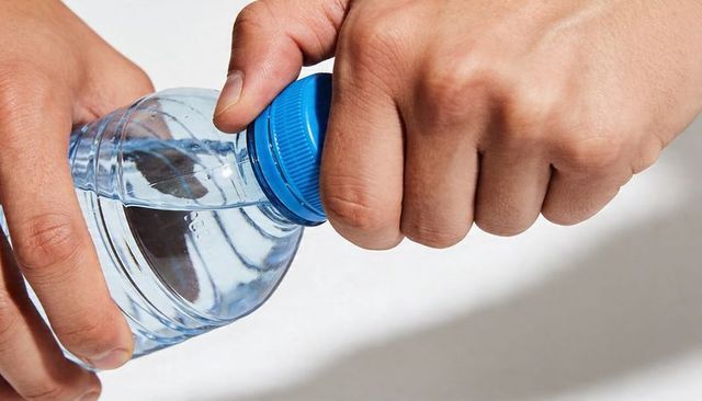 Closeup hands opening plastic water bottle with blue cap, clear water, daily hydration macro