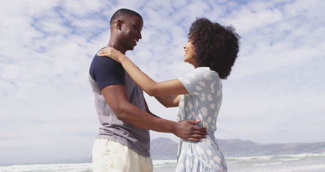 A young couple embracing and smiling on a sunny beach, enjoying their vacation. Perfect for content related to romance, travel, and carefree moments, as well as for advertisements focusing on relationship bliss and outdoor lifestyle.